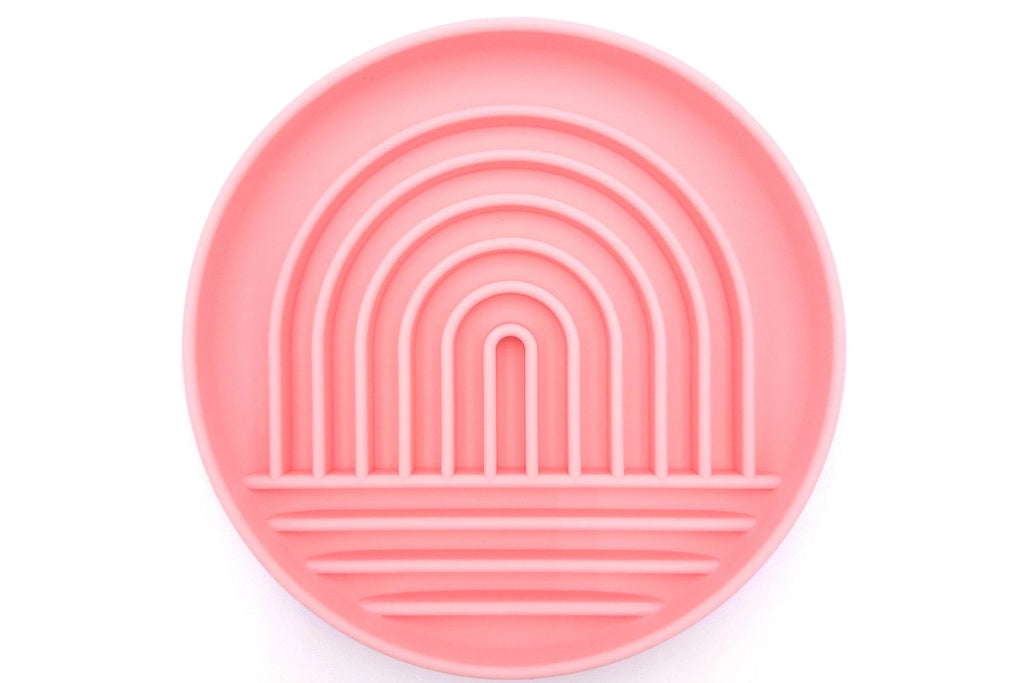 A round pink silicone plate with concentric rainbow arches and horizontal ridges, shown from a top-down view on a white background.